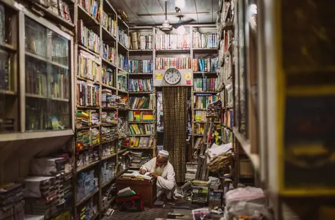A shopkeeper writing entries in a hand-written accounts ledger