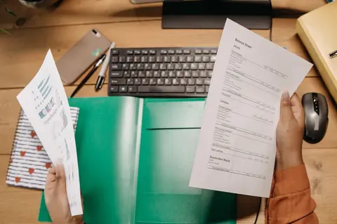 An accountant at a desk in India reviewing a printed balance sheet with a pen in hand.