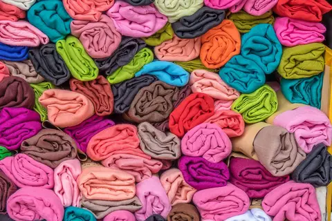 Rolls of colourful fabric stacked in an Indian textile shop, representing unsold closing stock.