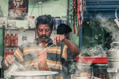 A small Indian tea stall with cups of chai and a vendor serving customers