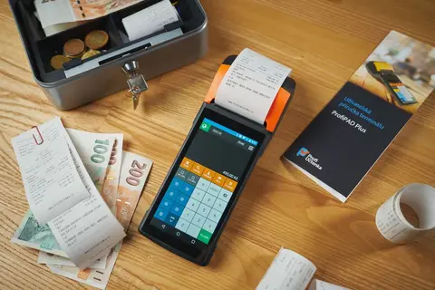 A small metal cash box next to a pile of paper receipts on an office desk