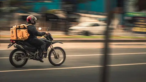 A delivery rider on a motorbike on a busy Indian city street, representing underemployment.