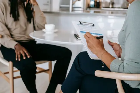 A person with a clipboard interviewing someone in an Indian neighbourhood.