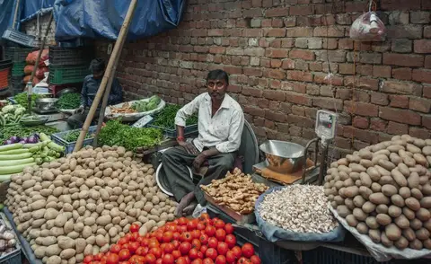 A busy Indian vegetable market with vendors and shoppers, showing everyday grocery shopping