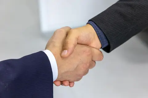 Two business partners shaking hands at a farewell meeting, representing a partner retiring from a firm.